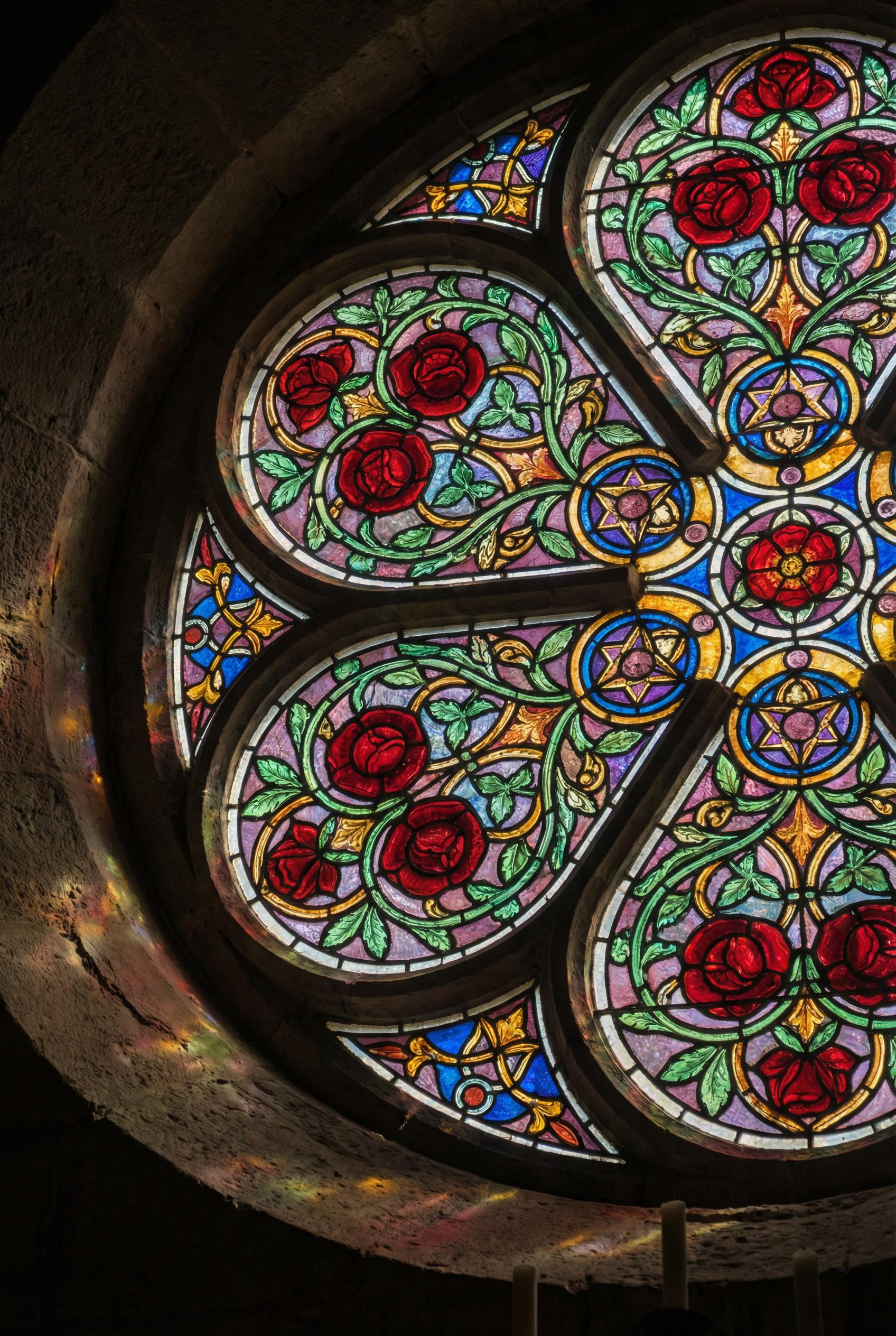A circular stained glass window design featuring intricate red roses and green vines, vibrant translucent colors, bold b