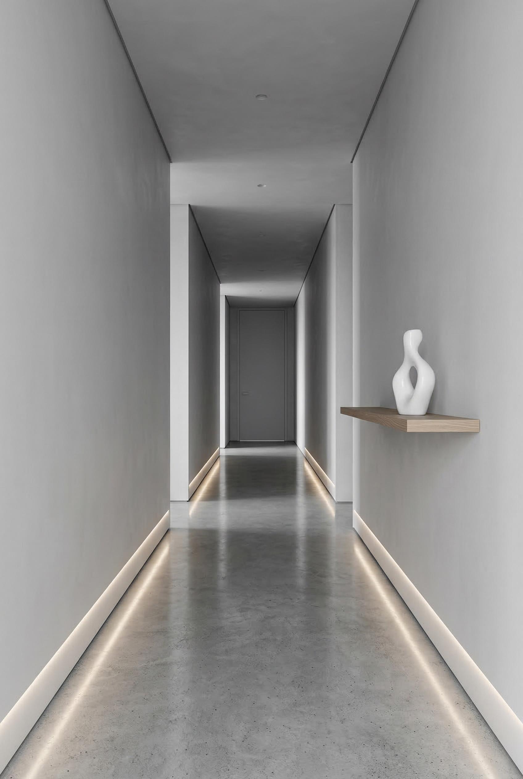 A monochrome minimalist hallway with polished concrete flooring reflecting subtle light, smooth pale grey plaster walls,