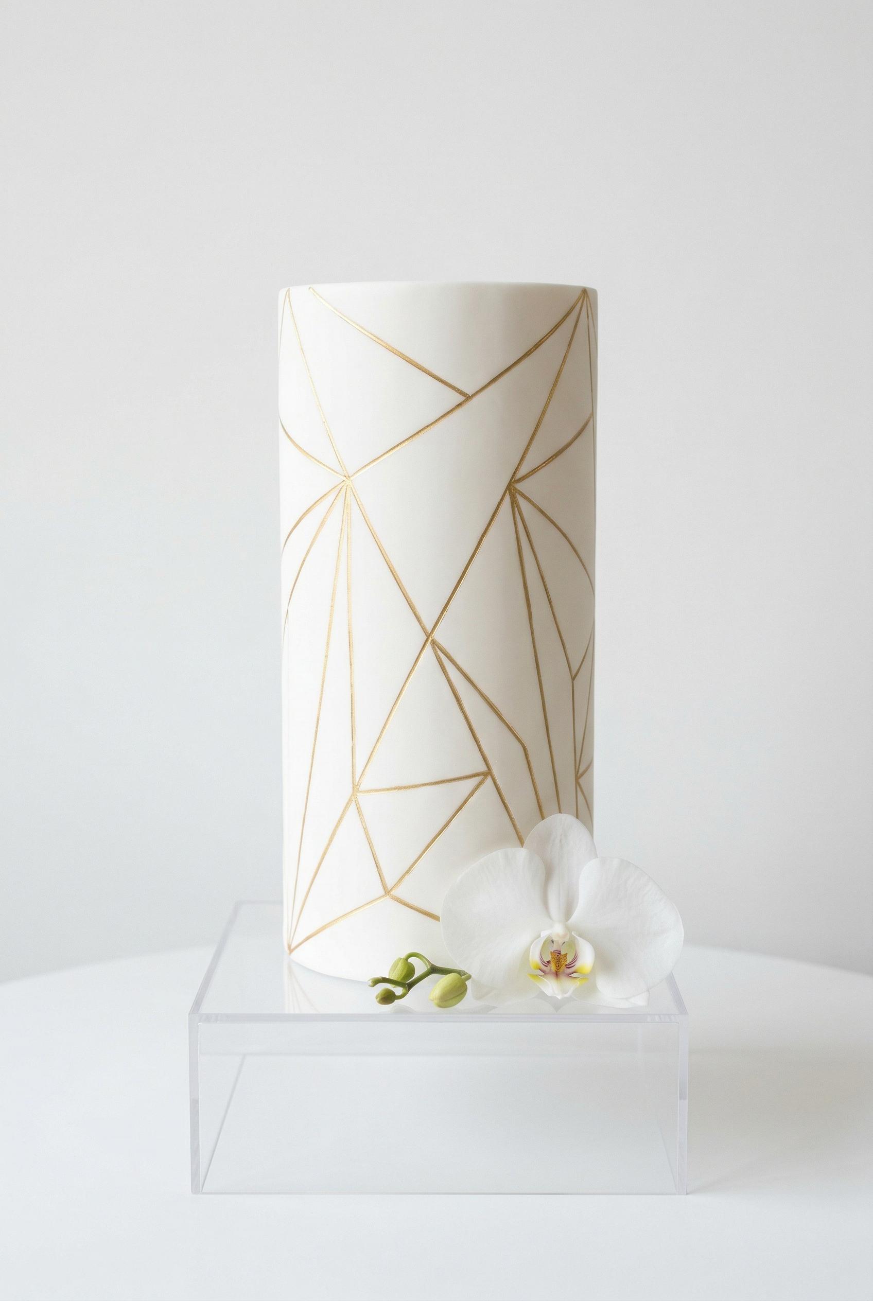A tall single-tier modern cylindrical wedding cake with perfectly smooth white fondant, decorated with precise thin gold