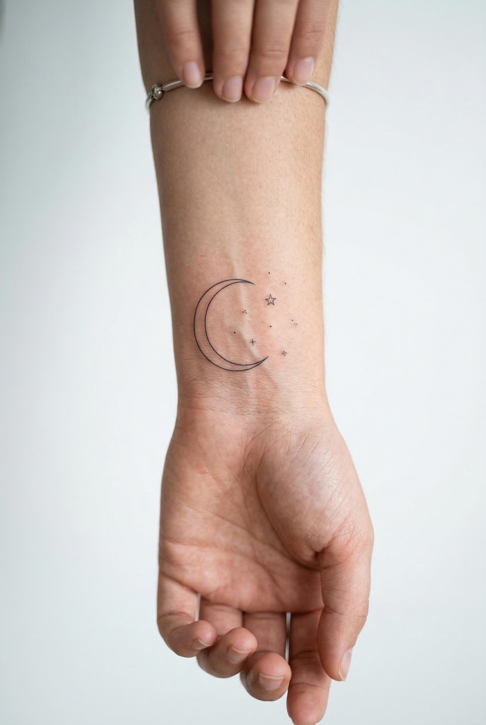 A delicate fine-line crescent moon tattoo with tiny scattered stars on the inner wrist, ultra-thin single-needle linewor