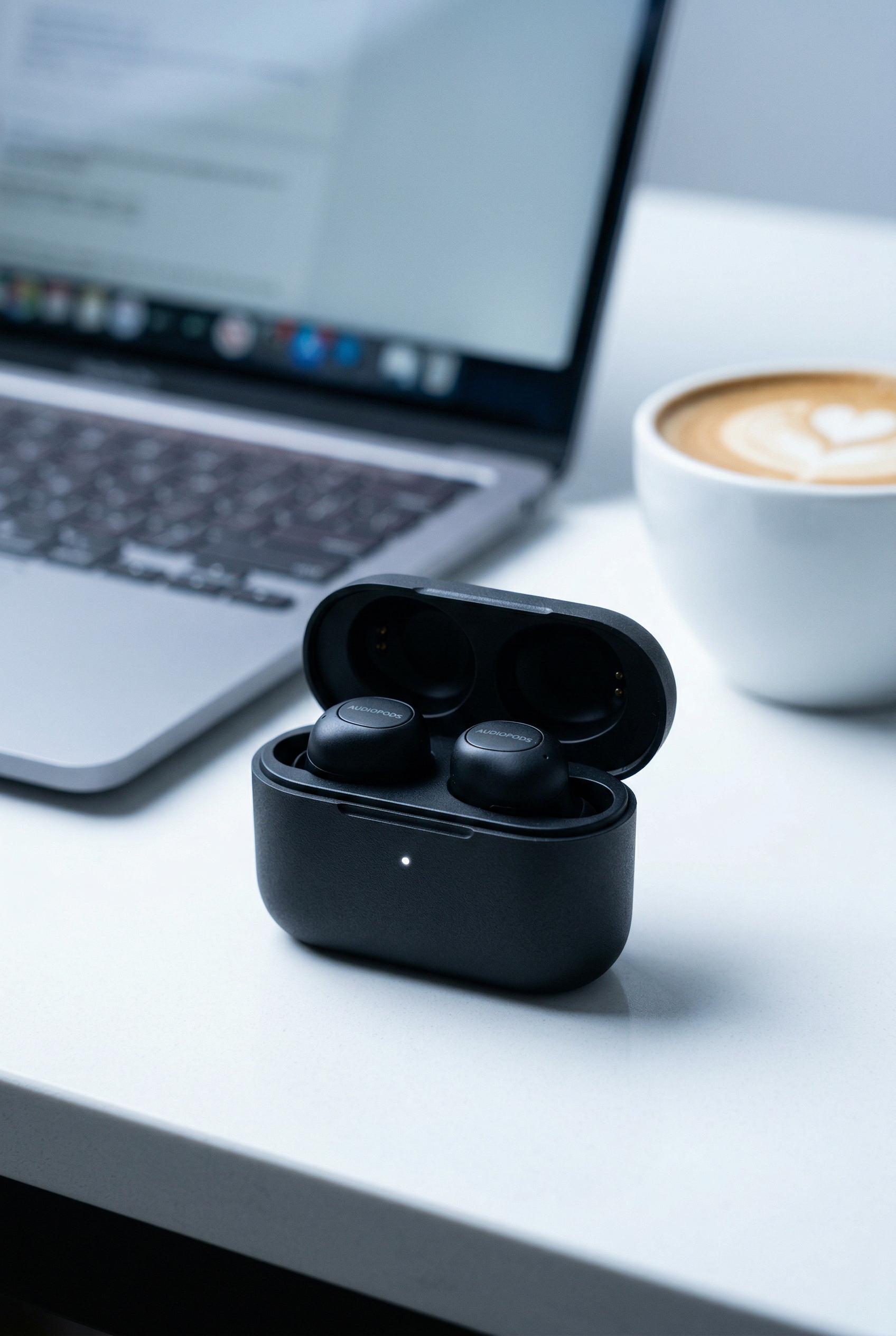 A pair of sleek wireless earbuds in a matte black charging case with a subtle LED indicator light, sitting on a clean wh