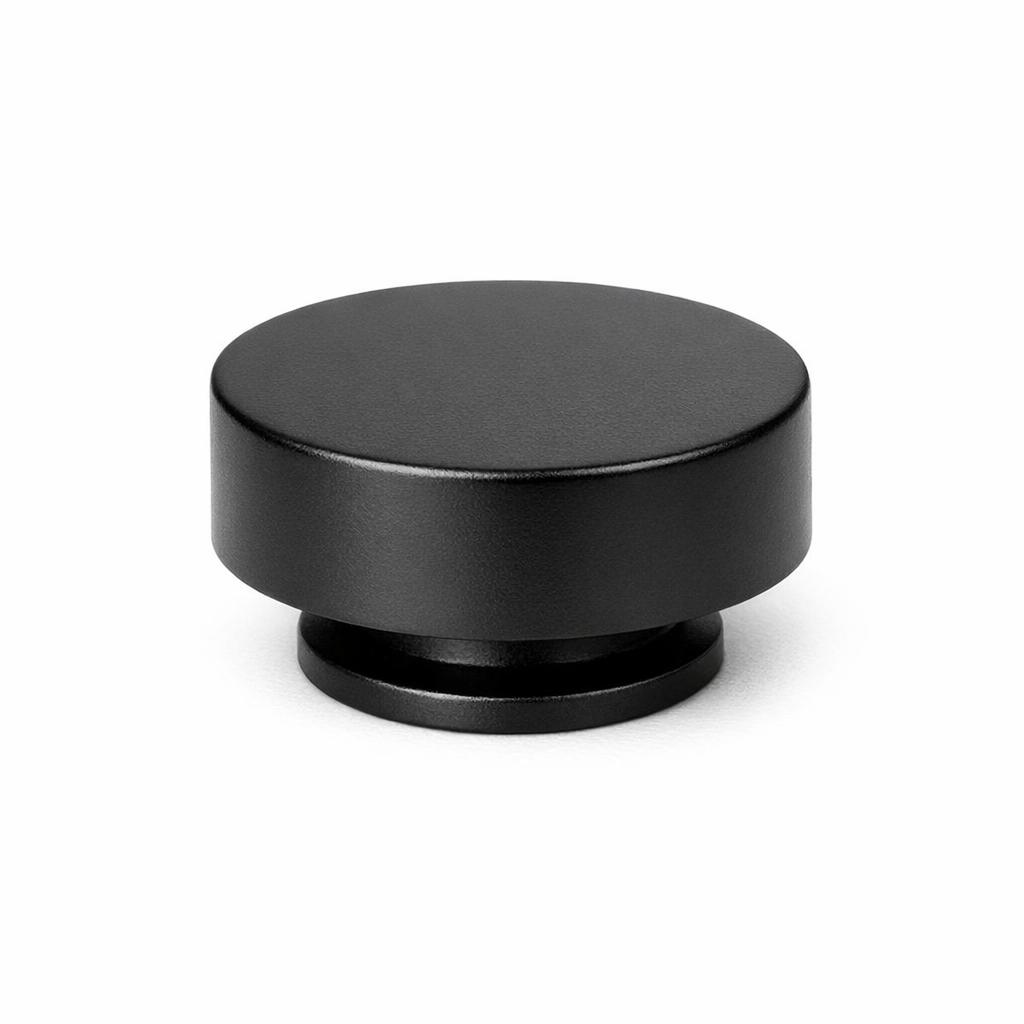 Commercial product photograph. A single residential cabinet knob. Smooth surface texture. Round Knob shape. Matte Black metal finish. Small circular base plate, single mounting post, approximately 1-1/4 inch diameter. Photographed on pure white seamless background (#FFFFFF). Studio softbox lighting, soft shadow directly underneath only. Macro lens, sharp focus throughout. Photorealistic real metal hardware. Not a 3D render. Not an illustration. Not CGI. Real cabinet hardware product photography quality. Variation 2: Paxton style cabinet knob: flat low cylindrical puck shape, completely flat top, no dome, straight vertical sides, sitting on a thin base ring, like a hockey puck. Smooth surface, no texture, no ribbing, no decorative details..