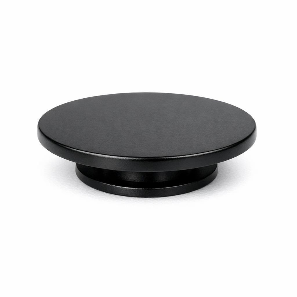Commercial product photograph. A single residential cabinet knob. Smooth surface texture. Round Knob shape. Matte Black metal finish. Small circular base plate, single mounting post, approximately 1-1/4 inch diameter. Photographed on pure white seamless background (#FFFFFF). Studio softbox lighting, soft shadow directly underneath only. Macro lens, sharp focus throughout. Photorealistic real metal hardware. Not a 3D render. Not an illustration. Not CGI. Real cabinet hardware product photography quality. Variation 3: Flat disc knob: very flat wide circular disc shape, almost no height, wide base. Low profile modern style..