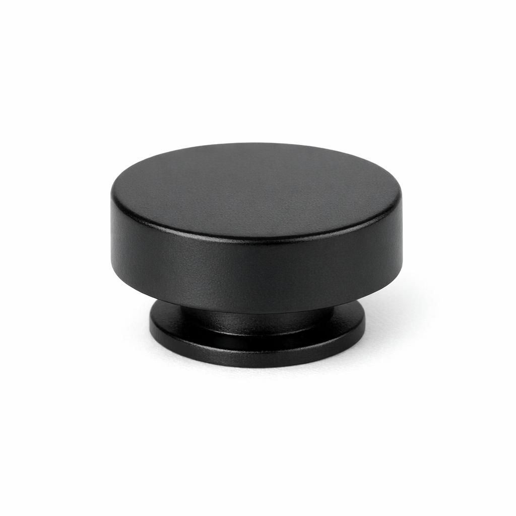Commercial product photograph. A single residential cabinet knob. Smooth surface texture. Round Knob shape. Matte Black metal finish. Small circular base plate, single mounting post, approximately 1-1/4 inch diameter. Photographed on pure white seamless background (#FFFFFF). Studio softbox lighting, soft shadow directly underneath only. Macro lens, sharp focus throughout. Photorealistic real metal hardware. Not a 3D render. Not an illustration. Not CGI. Real cabinet hardware product photography quality. Variation 2: Paxton style cabinet knob: flat low cylindrical puck shape, completely flat top, no dome, straight vertical sides, sitting on a thin base ring, like a hockey puck. Smooth surface, no texture, no ribbing, no decorative details..
