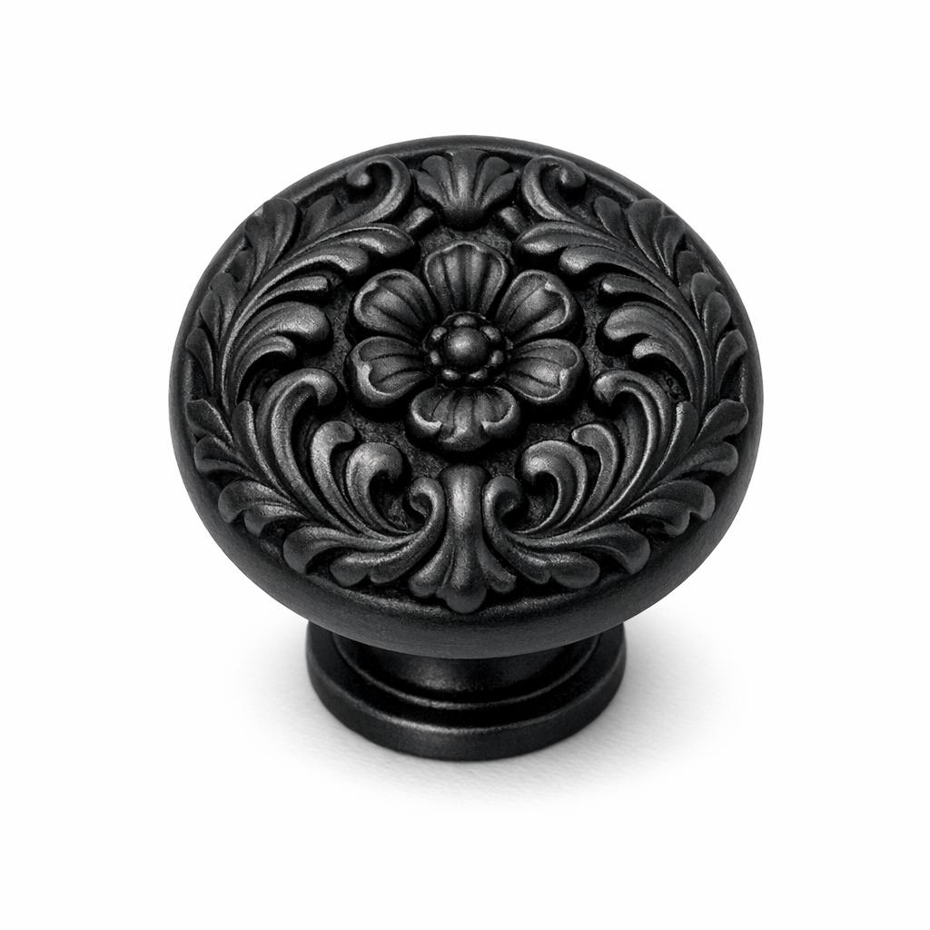 Commercial product photograph. A single residential cabinet knob. Floral surface texture. Round Knob shape. Matte Black metal finish. Small circular base plate, single mounting post, approximately 1-1/4 inch diameter. Photographed on pure white seamless background (#FFFFFF). Studio softbox lighting, soft shadow directly underneath only. Macro lens, sharp focus throughout. Photorealistic real metal hardware. Not a 3D render. Not an illustration. Not CGI. Real cabinet hardware product photography quality. Variation 9: Cabinet knob sculpted as an ornate Victorian acanthus leaf and flower cluster, scrolling sculpted leaves framing a central blossom, deep ornamental relief, small round base. Cast metal floral hardware..