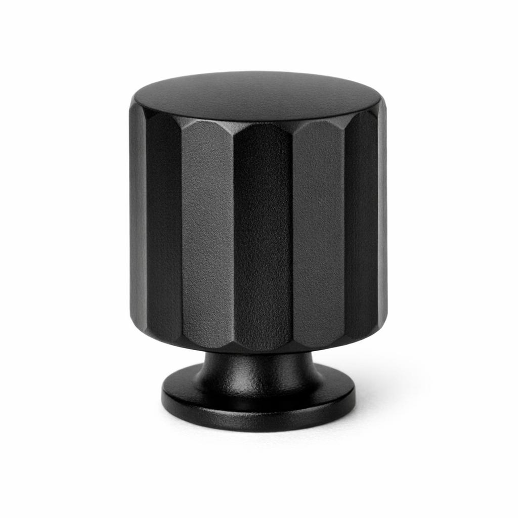 Commercial product photograph. A single residential cabinet knob. Faceted surface texture. Round Knob shape. Matte Black metal finish. Small circular base plate, single mounting post, approximately 1-1/4 inch diameter. Photographed on pure white seamless background (#FFFFFF). Studio softbox lighting, soft shadow directly underneath only. Macro lens, sharp focus throughout. Photorealistic real metal hardware. Not a 3D render. Not an illustration. Not CGI. Real cabinet hardware product photography quality. Variation 6: Freestone style cabinet knob: a tall vertical barrel with faceted flat planes cut around the full cylindrical body, sharp vertical edges, narrow base..
