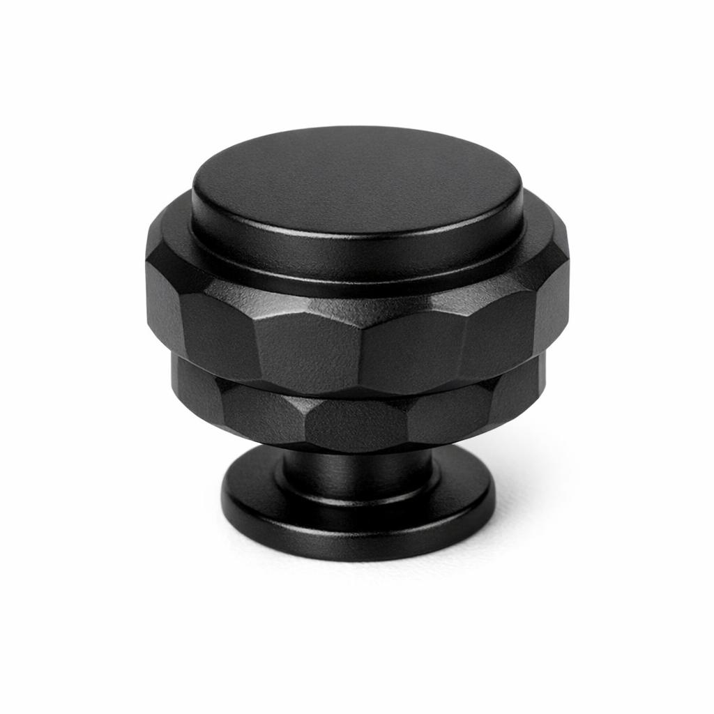 Commercial product photograph. A single residential cabinet knob. Faceted surface texture. Round Knob shape. Matte Black metal finish. Small circular base plate, single mounting post, approximately 1-1/4 inch diameter. Photographed on pure white seamless background (#FFFFFF). Studio softbox lighting, soft shadow directly underneath only. Macro lens, sharp focus throughout. Photorealistic real metal hardware. Not a 3D render. Not an illustration. Not CGI. Real cabinet hardware product photography quality. Variation 4: Cadet style cabinet knob: two-tier stacked cylinder with faceted angular cut planes around the body, flat top disc, three distinct stepped levels..