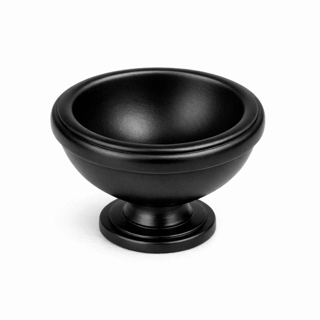 Commercial product photograph. A single residential cabinet knob. Smooth surface texture. Round Knob shape. Matte Black metal finish. Small circular base plate, single mounting post, approximately 1-1/4 inch diameter. Photographed on pure white seamless background (#FFFFFF). Studio softbox lighting, soft shadow directly underneath only. Macro lens, sharp focus throughout. Photorealistic real metal hardware. Not a 3D render. Not an illustration. Not CGI. Real cabinet hardware product photography quality. Variation 8: Cup knob: inverted dome or cup shape, hollow center visible from front, rim edge prominent, base plate. Traditional bin pull style knob..