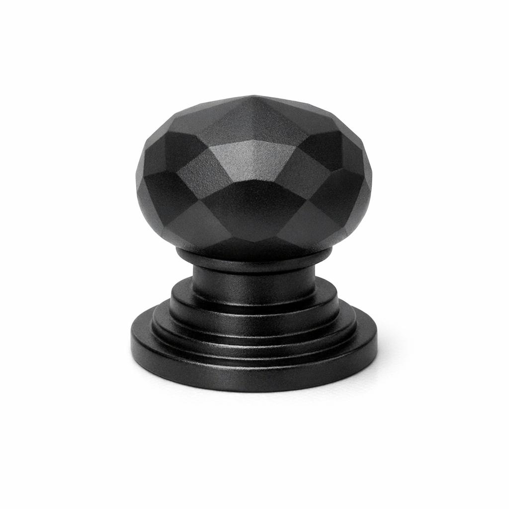 Commercial product photograph. A single residential cabinet knob. Faceted surface texture. Round Knob shape. Matte Black metal finish. Small circular base plate, single mounting post, approximately 1-1/4 inch diameter. Photographed on pure white seamless background (#FFFFFF). Studio softbox lighting, soft shadow directly underneath only. Macro lens, sharp focus throughout. Photorealistic real metal hardware. Not a 3D render. Not an illustration. Not CGI. Real cabinet hardware product photography quality. Variation 9: Podium style cabinet knob: a stepped pedestal of three tiers, the rounded top tier cut into angular gem-like facets, architectural stepped form..