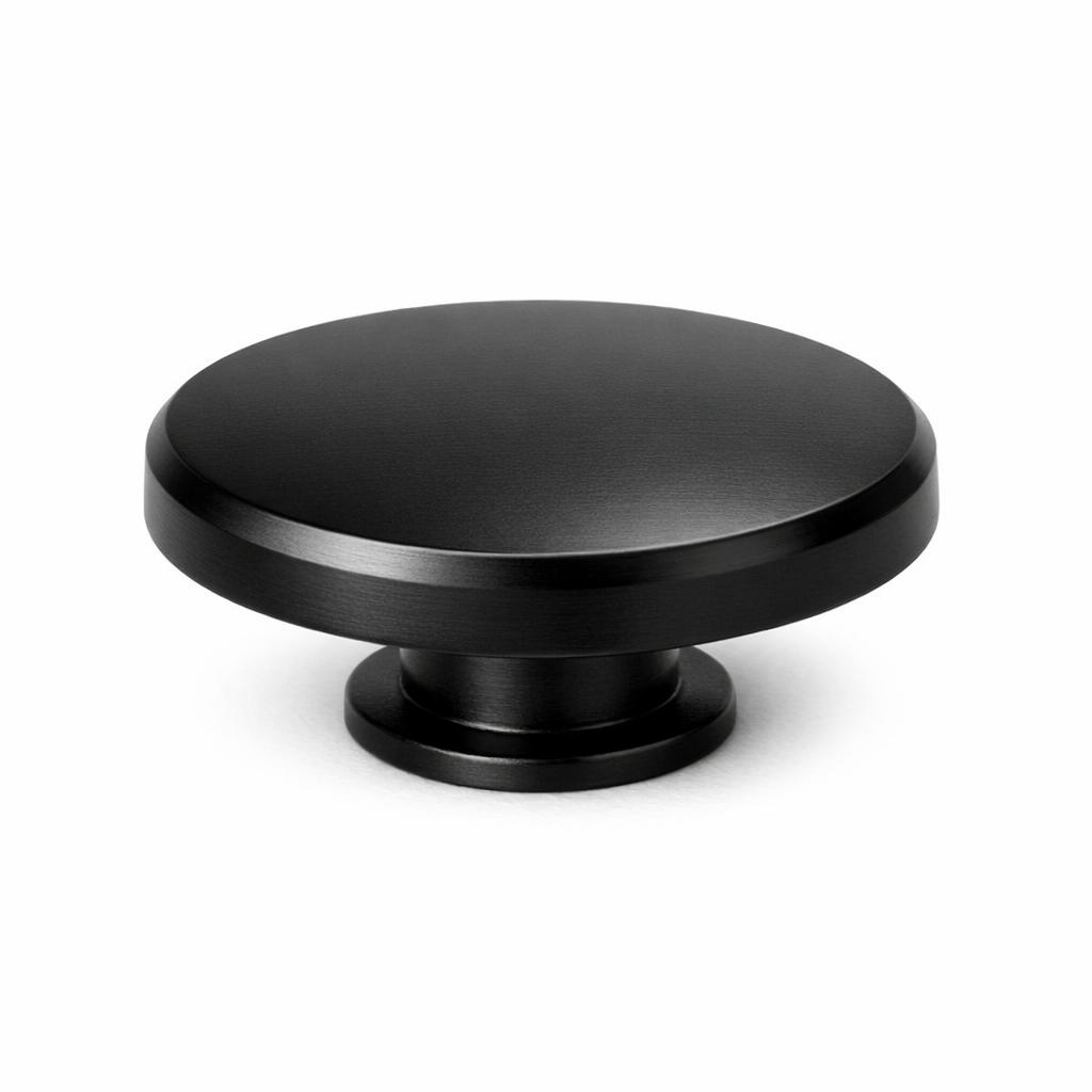 Commercial product photograph. A single residential cabinet knob. Smooth surface texture. Round Knob shape. Matte Black metal finish. Small circular base plate, single mounting post, approximately 1-1/4 inch diameter. Photographed on pure white seamless background (#FFFFFF). Studio softbox lighting, soft shadow directly underneath only. Macro lens, sharp focus throughout. Photorealistic real metal hardware. Not a 3D render. Not an illustration. Not CGI. Real cabinet hardware product photography quality. Variation 7: Rustic Modern style cabinet knob: a very wide shallow flat disc with a thick chamfered beveled edge, broad and low with minimal height. Smooth surface, no texture, no ribbing, no decorative details..
